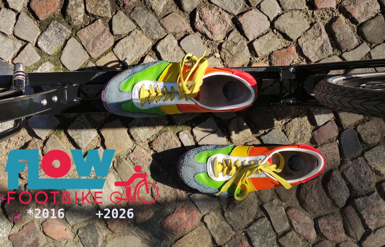Bunte Schuhe auf dem Trittbrett eines Tretrollers mit dem Text "Flow Footbike *2016  +2026"